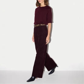 Model wearing Jigsaw burgundy wide-leg jumpsuit with short sleeves, styled with a leopard-print belt and black heeled boots.