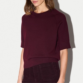 Model wearing Jigsaw burgundy short-sleeve knit top with ribbed hem, styled with dark corduroy trousers.