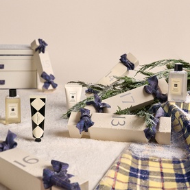 Jo Malone 25 Day Luxury Fragrance Advent Calendar with cream gift boxes, blue ribbon bows, fragrance bottles and festive greenery