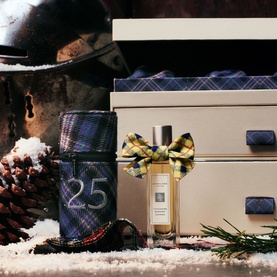 Jo Malone 25 Day Luxury Fragrance Advent Calendar with tartan wrapping, bow detail, and fragrance bottle, styled with pine cones and snow