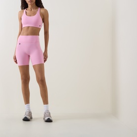 Model wearing On Running Bra in Magnolia pink, styled with matching pink cycling shorts, white socks and grey trainers