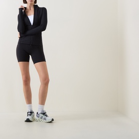 Model wearing On Running black fitted long-sleeve jacket with matching cycling shorts and white chunky trainers.