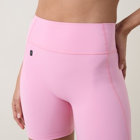 Model wearing On Running Magnolia pink high-waist cycling shorts with wide waistband and side pocket detail.