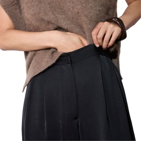 Model wearing Whistles black wide-leg trousers with front pleats, styled with a taupe knit top and dark bracelet.