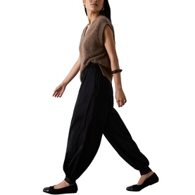 Model wearing Whistles black tapered harem trousers with elasticated hem, styled with a brown knit vest and black flat shoes.