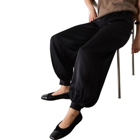 Model wearing Whistles black tapered trousers with elasticated ankles, styled with black ballet flats and a brown knit top.