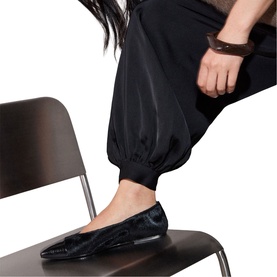 Model wearing Whistles black pointed-toe ballet flats with textured finish, styled with black tapered trousers and a brown leather cuff bracelet.
