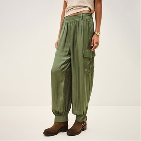 Model wearing Bash green satin cargo trousers with pleated front, side pockets, and elasticated ankles, styled with brown ankle boots