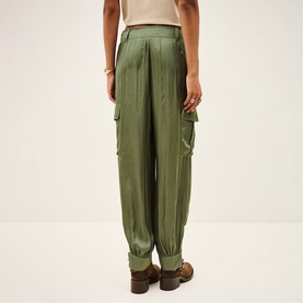Model wearing Bash green satin cargo trousers with pleated front, elasticated cuffs, and side pockets, styled with brown leather loafers