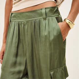 Model wearing Bash green satin wide-leg trousers with pleated waist and side pockets, styled with gold cuff bracelet