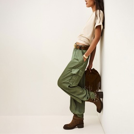 Model wearing Bash green cargo trousers with cream T-shirt and brown belt, styled with a fringed suede bag and tan ankle boots