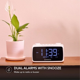 Roberts Ortus 4 FM Dual Alarm Clock Radio in white, displaying time on blue LED screen, styled on wooden shelf beside plant