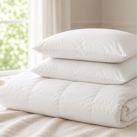 The Soft Bedding Co duvet in white, neatly rolled and displayed with two stacked white pillows on a bed