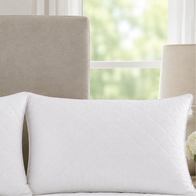 The Soft Bedding Co white quilted pillow styled on a bed with a neutral upholstered headboard and soft lighting.
