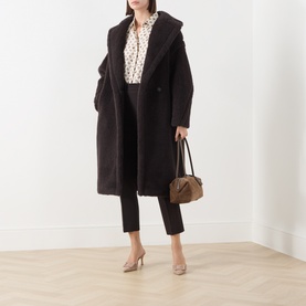 Model wearing Max Mara dark brown alpaca wool blend teddy coat, styled with printed blouse, cropped trousers, nude heels, and tan handbag.