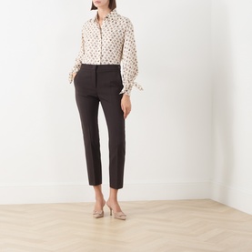 Model wearing Max Mara Main dark brown slim-leg wool trousers, styled with a cream polka dot blouse and nude heels.