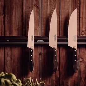 Tramontina stainless steel kitchen knives with black handles mounted on a magnetic wooden wall strip, herbs visible below