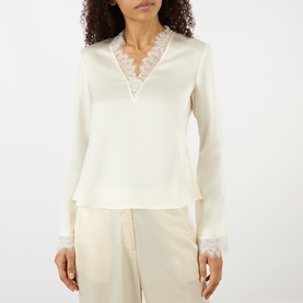 Model wearing Ganni Egret blouse with V-neck lace trim detail and lace cuffs, styled with matching wide-leg trousers
