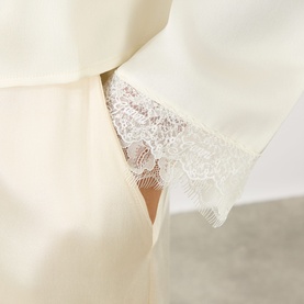 Ganni blouse in Egret, close-up of delicate lace trim detail at hem on satin-finish fabric