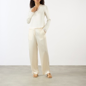 Model wearing Ganni Egret blouse with long sleeves, styled with cream wide-leg satin trousers and beige strappy sandals.