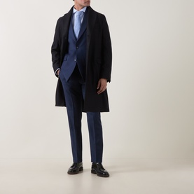 Model wearing Tiger of Sweden Sea suit trousers styled with a navy overcoat, blue waistcoat, light blue shirt and black leather shoes.