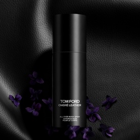 Tom Ford Ombr&eacute; Leather All Over Body Spray in black bottle, styled with purple flowers on dark leather backdrop