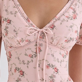 Model wearing House of CB Pink Vintage Rose floral dress with V-neckline, lace trim, ribbon tie detail and short puff sleeves