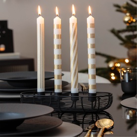 Villeroy & Boch striped taper candles in cream and gold, lit and displayed in a black wire holder on a dark festive table