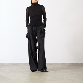 Model wearing MeiMeij Nero sheer mesh turtleneck top with long sleeves, styled with wide-leg black cargo trousers and black flat shoes.