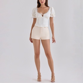 Model wearing House of CB ivory puff-sleeve crop top with lace-up neckline, styled with cream mini shorts and nude heeled sandals.