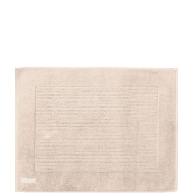 Pale blush rectangular bath mat with ribbed border detail and small woven brand label on lower left corner