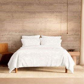 White floral jacquard duvet cover set styled on a low wooden bed frame in a minimalist neutral bedroom setting