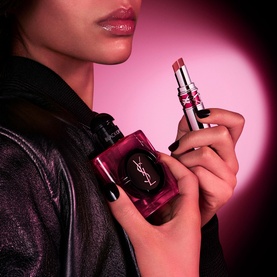 Model with YSL Black Opium Pink Glaze Eau De Parfum bottle, holding a pink lip product against a glowing pink background