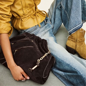 Model carrying Bash purple suede drawstring bag with gold chain detail, styled with yellow top and blue jeans