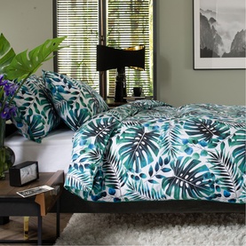White duvet set with green and teal tropical leaf print, styled on a dark bed frame with matching pillowcases in a bedroom setting.
