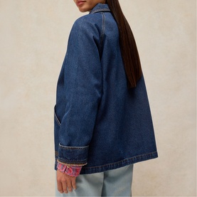 Model wearing White Stuff mid denim jacket with pink embroidered cuff detail, shown from behind, styled with light blue jeans.
