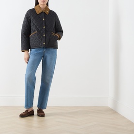 Model wearing Barbour black quilted coat with corduroy collar, styled with light blue jeans and brown loafers