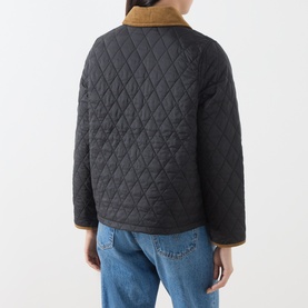 Model wearing Barbour black quilted jacket, rear view, with tan corduroy collar, styled with blue jeans.