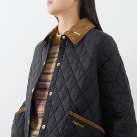 Model wearing Barbour black quilted coat with tan corduroy collar and gold buttons, styled over a multicolour striped knit