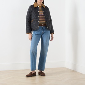 Model wearing Barbour black quilted jacket with tan collar, styled with striped jumper, blue straight-leg jeans and brown loafers