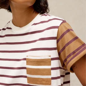 Model wearing White Stuff ivory stripe T-shirt with contrast tan sleeves, chest pocket, and burgundy stripe detail, close-up view.
