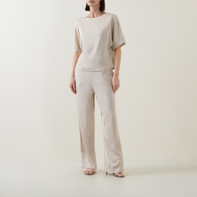 Model wearing FeeG champagne short-sleeve top with wide-leg trousers and strappy heeled sandals.
