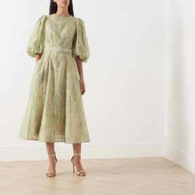 Model wearing FeeG Green Print midi dress with puff sleeves and belted waist, styled with gold heeled sandals.