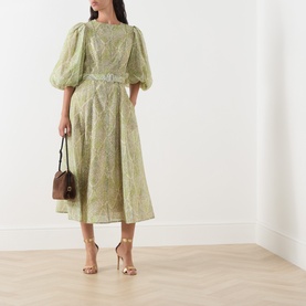 Model wearing FeeG Green Print midi dress with puff sleeves and belt, styled with gold heeled sandals and brown mini bag.