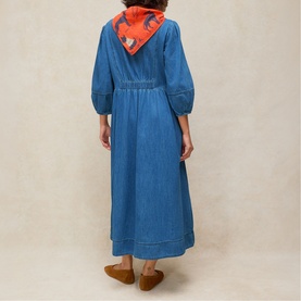 Model wearing White Stuff mid denim midi dress with balloon sleeves, styled with an orange printed scarf and tan flat shoes, back view.