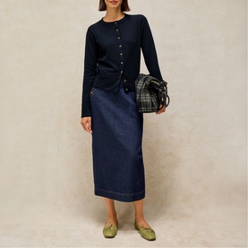 Model wearing White Stuff dark navy midi denim skirt with navy cardigan, styled with a plaid bag and green flat shoes.