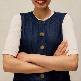 Model wearing White Stuff dark denim sleeveless button-front dress over a white short-sleeve top, arms crossed.