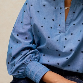 Model wearing White Stuff blue multi polka dot blouse with V-neckline, long sleeves and chambray cuffed detail, styled with a silver necklace.
