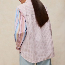 Model wearing White Stuff shirt in pink multicolour stripe, rear view, loose fit, paired with light blue trousers