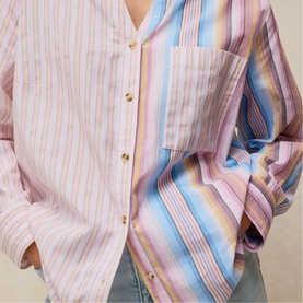 Model wearing White Stuff pink multicolour striped shirt with chest pocket and gold buttons, styled with light blue trousers.